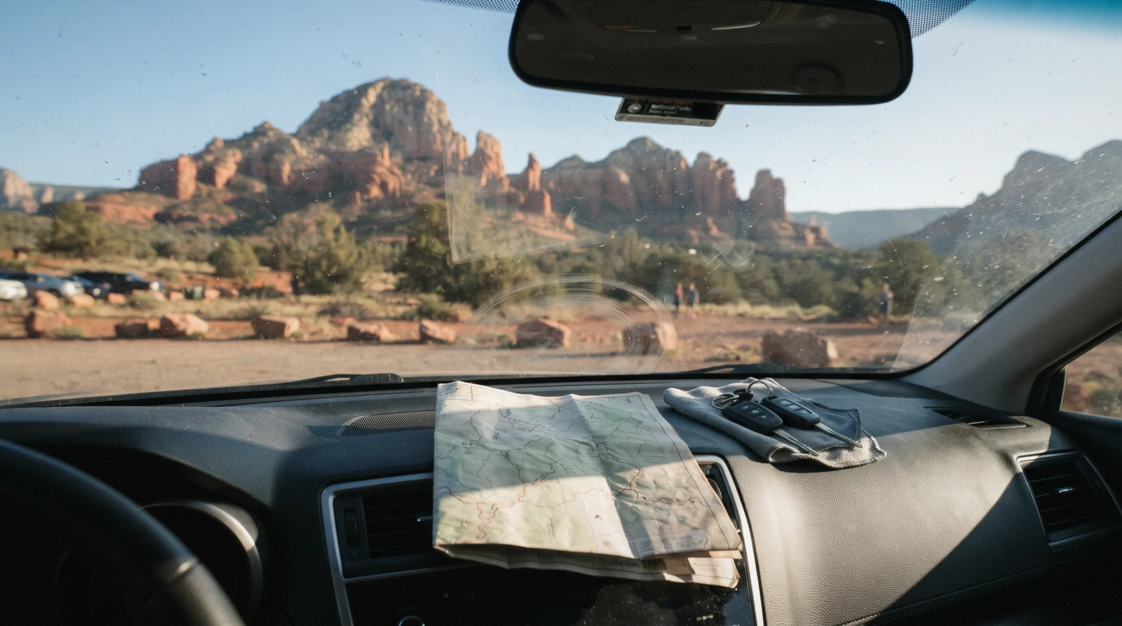 A car pulled off a red-dirt Sedona road with red rock formations spread out in the distance, the view that Sedona trip planning has to account for