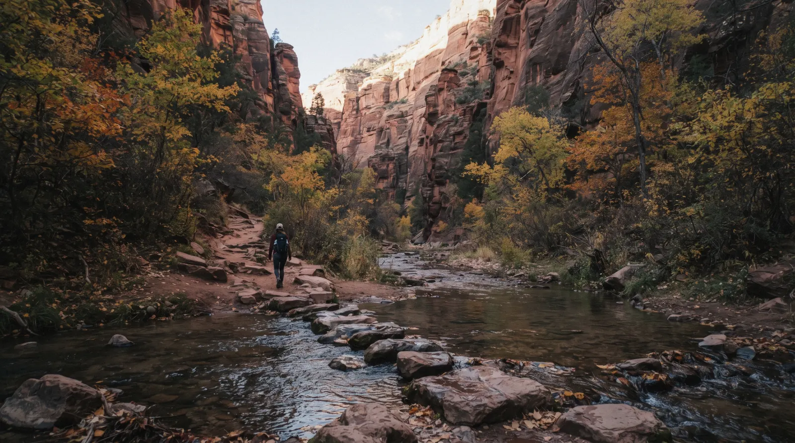 Hikers crossing Oak Creek on stepping stones beneath tall canyon walls on the West Fork Trail in Sedona's Oak Creek Canyon